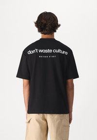 Camiseta de algodón negra con un atrevido texto blanco en la parte posterior: "no desperdicies la cultura" y "MAISON D'ART". Mangas cortas, corte relajado.