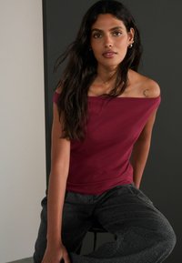 Vīna sarkanā off-shoulder blūze, mīksta auduma, pieguļoša dizaina. Pelēkas tekstūrētas bikses ar plašu kāju, ar smalku zivs kaula rakstu.