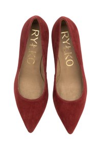 Bailarinas rojas de ante con punta afilada y un interior suave, decoradas con un logotipo dorado embossado. El diseño presenta lados bajos para una silueta elegante.