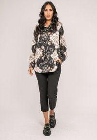 Blouse noire et crème à motifs avec des designs floraux et géométriques, associée à un pantalon noir court et des mocassins noirs avec des accents en matériel doré.