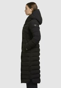 Cappotto puffer nero con silhouette allungata, dotato di un grande cappucci, tasche con zip e sezioni trapuntate testurizzate in tutto il capo.