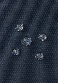 Klare Wassertropfen auf einem strukturierten dunkelblauen Stoff, variierend in Größe und Form, die ihre runden Formen und reflektierenden Oberflächen hervorheben.