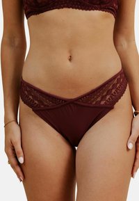 Bas de bikini bordeaux avec dentelle, au design croisé, présentant des motifs en diamant élaborés le long de la ceinture et un tissu lisse.