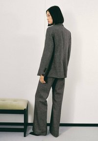 Traje de mezcla de lana gris que incluye un blazer ajustado y pantalones de pierna ancha, con una textura suave y detalles de costura sutil, sobre un fondo neutro.