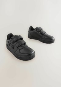 Baskets noires en cuir avec une finition lisse, dotées de deux sangles Velcro réglables et d'une semelle en caoutchouc texturé.
