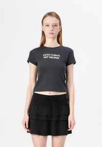 Black cropped t-shirt with white text "CATCH FLIGHTS NOT FEELINGS" on the front, paired with a layered black mini skirt.