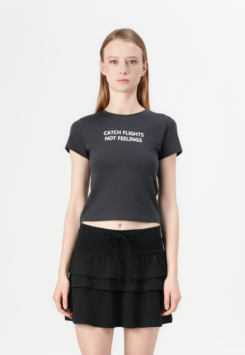 Black cropped t-shirt with white text "CATCH FLIGHTS NOT FEELINGS" on the front, paired with a layered black mini skirt.