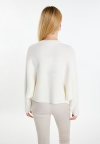 Witte geribbelde trui met verlaagde schouders, met een losse pasvorm en een afgeronde zoom, gecombineerd met lichtbeige broeken. Zachte textuur.