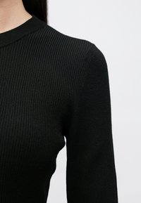 Pulover negru cu dungi, prevăzut cu guler rotund și mâneci lungi, care evidențiază un material texturat și o siluetă conică.