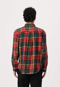 Camicia a quadri rossa, verde e gialla con maniche lunghe e orlo arrotondato. Presenta un colletto e polsini con bottoni.
