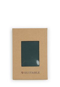 Donkergroen stoffenstaal verpakt in een rechthoekige kraftpapieren verpakking met een doorzichtige venster en het "SUITABLE" logo in donkerblauw gedrukt.