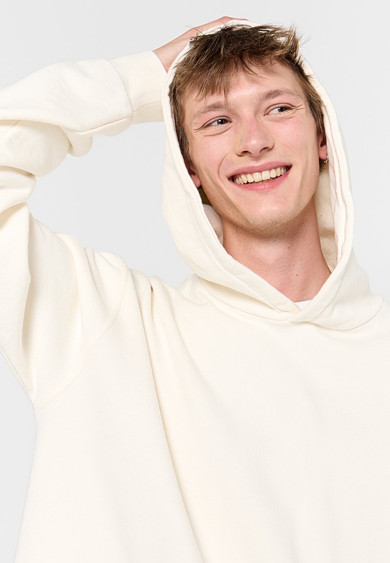 Cremfarbene Kapuzenjacke aus weichem Stoff mit großer Fronttasche, weiten Ärmeln und Kapuze mit Kordelzug.