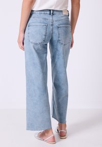 Vaaleansiniset väljät farkut, joissa on kulunut pesu, kaksi takataskua, revitty helma ja keskikorkea vyötärö. Materiaalin näyttää olevan pehmeää farkkukangasta.