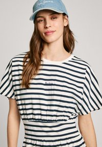 Dryžuota suknelė su tamsiai mėlynomis ir baltomis horizontalinėmis juostelėmis, trumpomis rankovėmis, surinkta juosmeniu ir apvaliu iškirpimu. Kepurė su šviesiu džinsiniu audiniu ir tekstu.