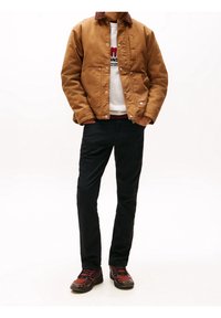Chaqueta de lona marrón con cuello de pana, sobre un sudadera blanca, combinada con pantalones negros y zapatillas rojas y negras.