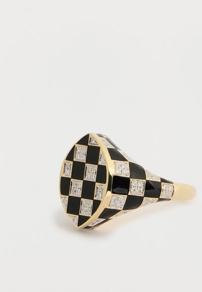 Zlatý prsteň v trojuholníkovom tvare s šachovnicovým vzorom čierneho smaltu a čírych kameňov, vytvárajúci textúrovaný geometrický dizajn.