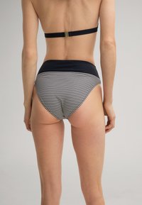 Achteraanzicht van een persoon in een zwart-wit gestreepte high-waisted bikini onderkant en een zwarte bikini top met een haaksluiting.