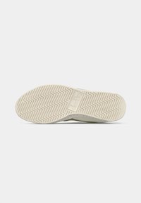 Rubber shoe outsole with a textured, zigzag pattern. Color is light beige with branding visible in the center. Flat shape designed for traction.