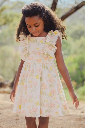Vestido de algodão floral com detalhes em rufos nos ombros, apresentando tons pastéis de rosa, amarelo e verde sobre um fundo branco. Design curto e evasé.