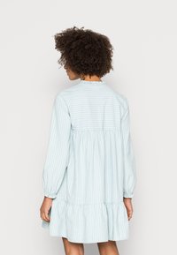 Vestido azul claro com riscas, mangas longas, cintura franzida e bainha com babados. O tecido parece macio e texturizado, com um detalhe de decote redondo.