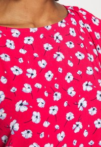 Blumenkleid mit einem leuchtend pinken Hintergrund, auf dem weiße Blumen mit schwarzen Zentren über den Stoff verteilt sind. Glatte Textur, runder Ausschnitt.
