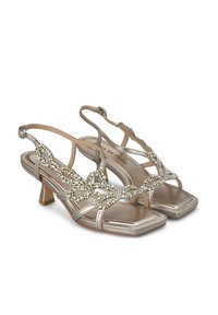 Sandali metallici oro con tacco medio, caratterizzati da un dettagliato copricatena in cristallo e da sottili cinturini con design aperto sulla punta.
