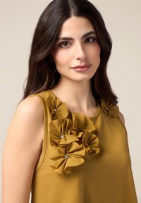 Top senza maniche giallo senape con fiori in tessuto tridimensionale e centro gioiello sul collo. Tessuto liscio e texturizzato.