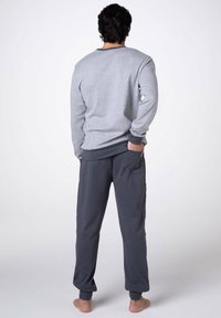 Felpa grigia e pantaloni della tuta grigio scuro visti da dietro; vestibilità comoda, tessuto morbido, con polsini ai polsi e alle caviglie, e tasche laterali.