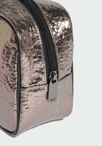 Metalna ružičasta kozmetička torbica s teksturiranim završetkom, crnim patentnim zatvaračem i srebrnim vućem s detaljem logotipa. Zaobljeni oblik.