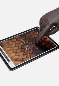 Brun læderhandske rører ved en tablet-skærm, der viser et struktureret, brunt, vævet mønster. Tablet'en har en sort ramme og en klar grænseflade.