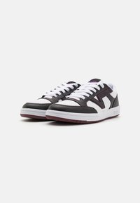 Black and white sneakers with a smooth leather upper, white laces, purple accents, and a textured rubber sole. Rounded toe design.