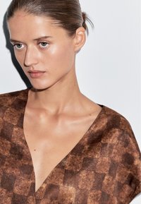 Brunblomstret bluse med dyb V-hals og blødt stof, der har et ternet design og en afslappet pasform.