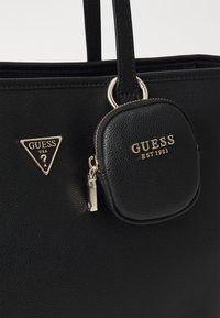 Svart teksturert lær tote bag med et gullfarget tredimensjonalt logo og en avtagbar myntlomme, med gullglidelås og merkevaredetalj.
