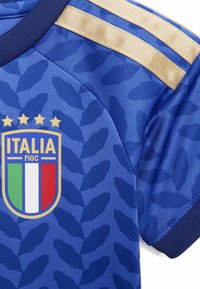 Camiseta de fútbol azul de Italia con franjas doradas en el hombro y el escudo de la FIGC de Italia que presenta cuatro estrellas doradas y los colores de la bandera italiana.