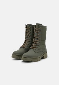 Bottes montantes lacées vert olive avec panneaux matelassés, semelles épaisses en caoutchouc et lacets bruns. Matériau imperméable durable, conception robuste.