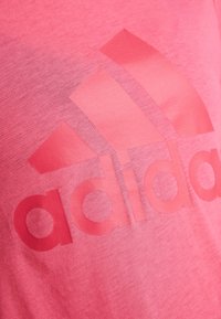 Camiseta rosa de algodón, con un gran logo tonal de Adidas en una tonalidad más oscura de rosa, con una textura suave y un ajuste informal.