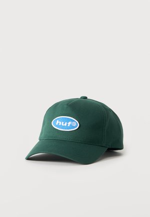 Casquette de baseball vert foncé avec visière courbée et écusson logo bleu « "huf" » sur le devant, présentée sur un fond uni clair.