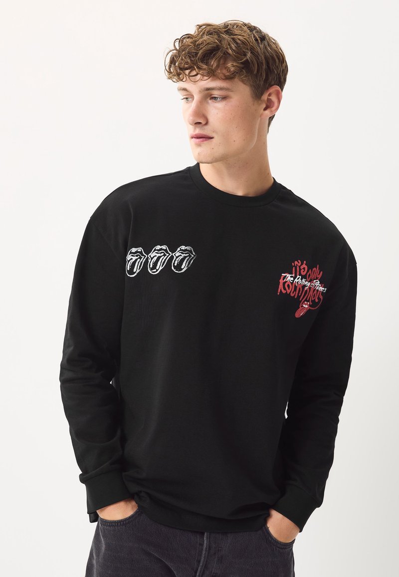 Sort langærmet t-shirt lavet af bomuld, med broderet Rolling Stones læbelogo i hvidt og rødt på brystet, ribstrikkede manchetter.