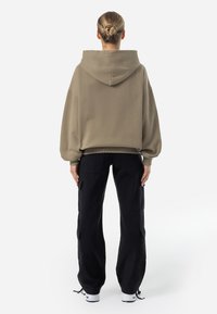 Felpa oversize color khaki con cappuccio regolabile e polsini a coste, abbinata a pantaloni cargo neri con tasche laterali e vestibilità comoda.