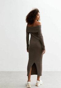 Khaki-ripptes Strickkleid mit schulterfreiem Ausschnitt, langen Ärmeln und einem Rückenschlitz, kombiniert mit weißen Sneakers.