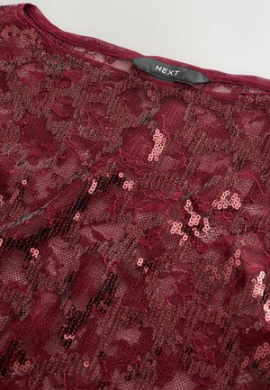 Top en dentelle bordeaux avec des sequins, présentant une texture douce et un motif floral. L'étiquette indique "NEXT" au niveau du col.