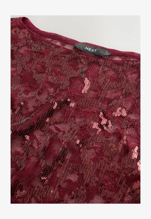 Top en dentelle bordeaux avec des sequins, présentant une texture douce et un motif floral. L'étiquette indique "NEXT" au niveau du col.