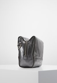 Czarna skórzana torba o usztywnionym kształcie, zamykana na zamek błyskawiczny, z akcentami w kształcie uszu kota na górze. Gładka tekstura z delikatnym połyskiem, wyposażona w metalowe okucia.