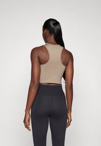 Brun cropped tank top med racerback-design, kombinert med høytlivs svarte leggings, som viser en tettsittende silhuett og jevn tekstur.
