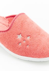 Zapatilla de coral con tejido texturizado, borde elástico, suela blanca y detalles de estrellas plateadas en el costado. Diseño de talón cerrado para mayor comodidad.