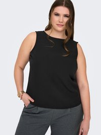 Donna che indossa una maglietta nera senza maniche e pantaloni grigi, con un braccialetto d'oro sul polso sinistro e capelli mossi sciolti.