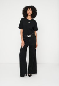 Črno preveliko majico z logotipom, kombinirano z visokim pasom črnih širokih hlač in črnim pasom s srebrno ovalno sponko.