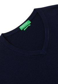 Granatowy sweter z dekoltem w serek, wykonany z miękkiego materiału. Posiada żebrowany dekolt oraz zieloną metkę z logo przy kołnierzu. Ogólnie gładka faktura.