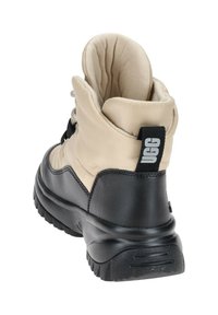 Botín de tobillo de nylon beige acolchado con suela de goma negra, cierre de cordones y una lengüeta con marca en la parte posterior para facilitar su uso.