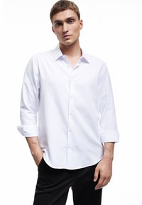 Witte lange mouwen blouse met een klassieke kraag, een gladde textuur en opgerolde manchetten, gecombineerd met zwarte broek.